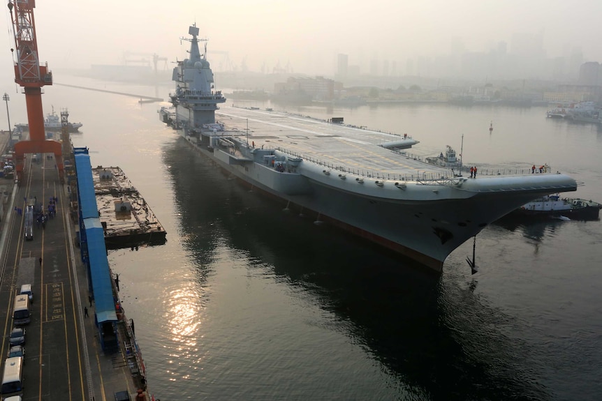 China's first domestically developed aircraft carrier departs Dalian port. It is smoggy, but you can see distant skyscrapers.