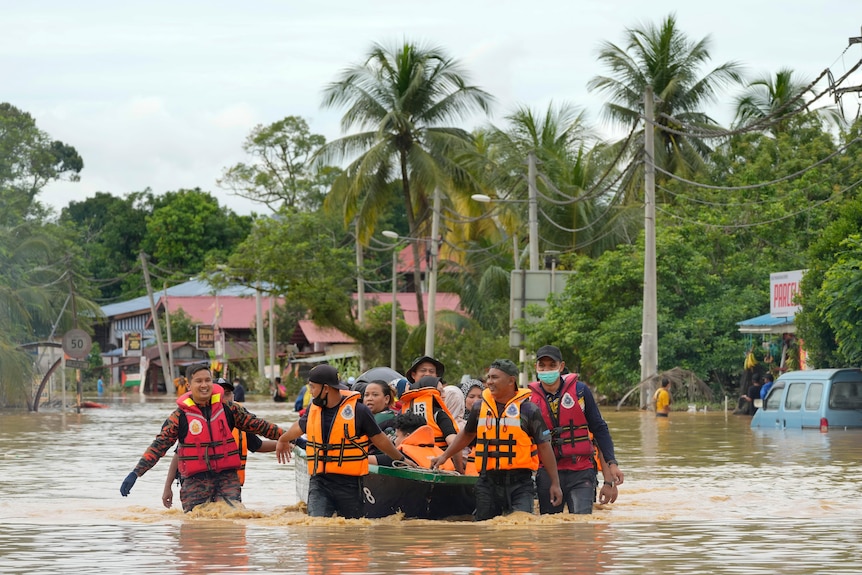 Los salvavidas y otras personas con chalecos salvavidas guían y se sientan en un bote pequeño mientras algunos lo arrastran a través de las inundaciones marrones hasta las rodillas.