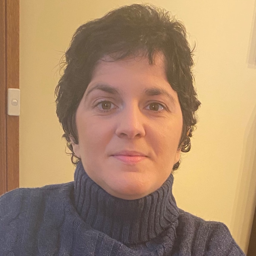 Woman with short dark hair smiling with a wall and door frame behind her.