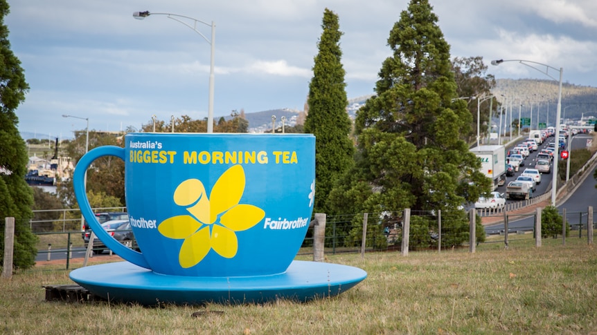 A giant blue tea cup and saucer on a lawn near a highway.