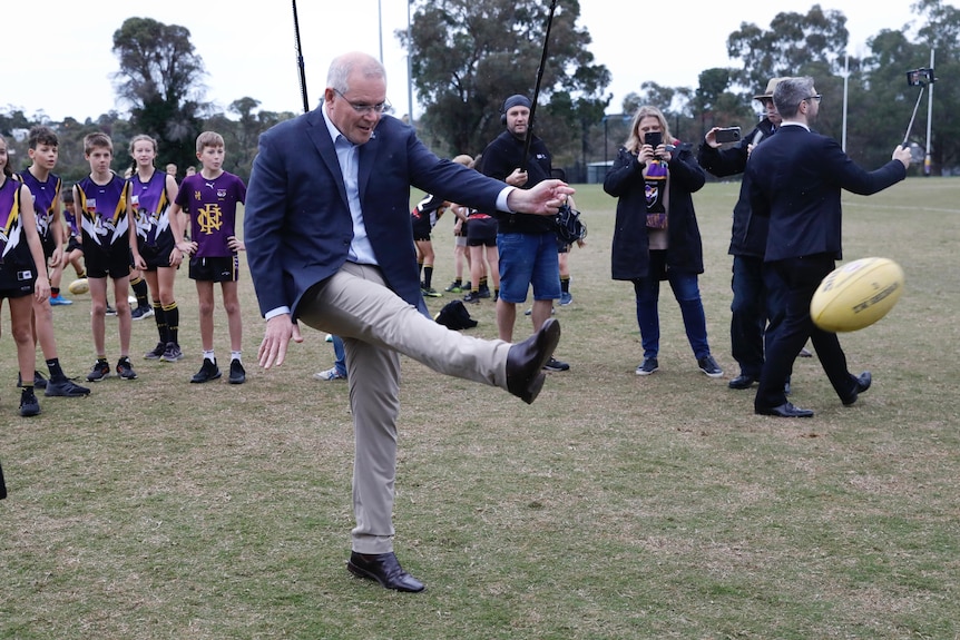 Prime Minister Scott Morrison kicks a football in front of children, media