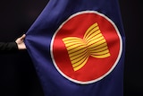 a hand pulls out the ASEAN flag for a camera against a black background