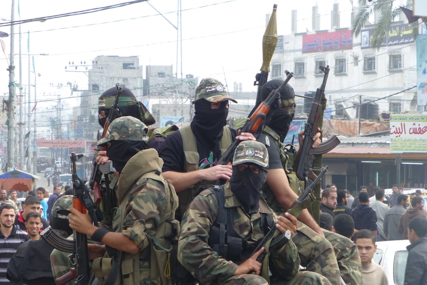 Soldiers holding guns and wearing balaclavas amid crowd in Gaza street.