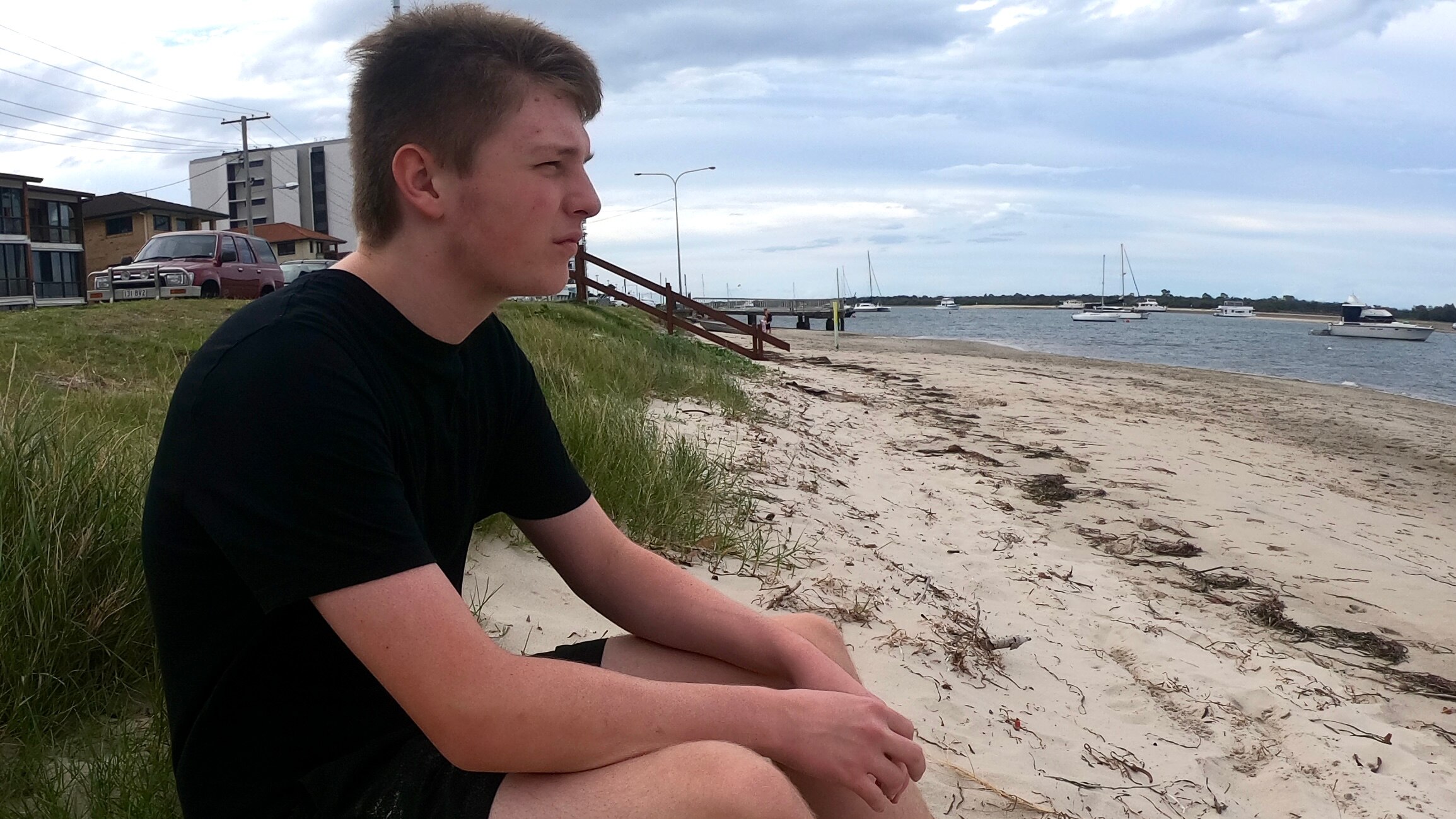 A young man sitting on the beach staring at the ocean.