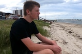 A young man sitting on the beach staring at the ocean.