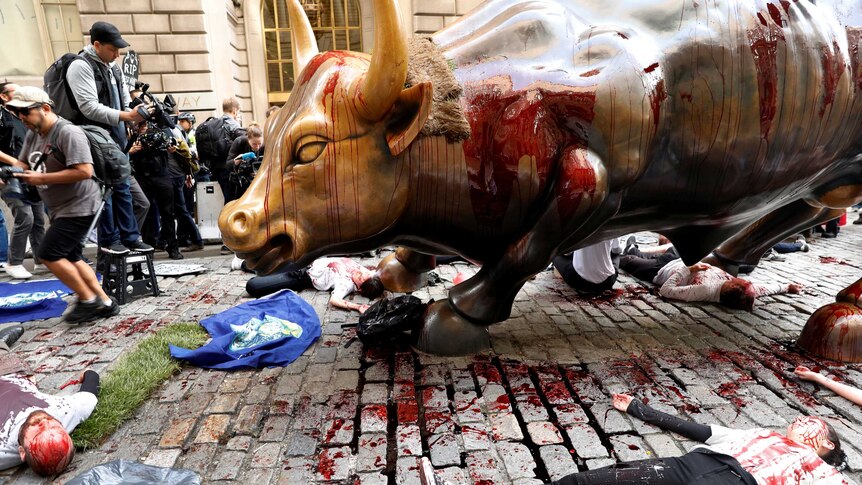 Climate change activists lay on the ground covered in fake blood at the feet of the Wall Street Bull statue.