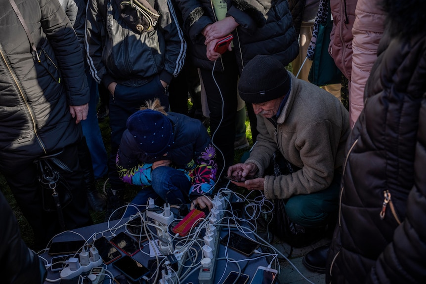 A group of people gathering around an internet hotspot and powerbank on the ground.