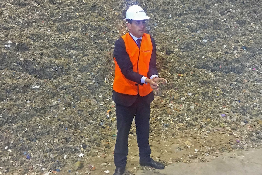 Tom Koutsantonis in orange vest and hard hat holds some waste destined to be used for industrial fuel