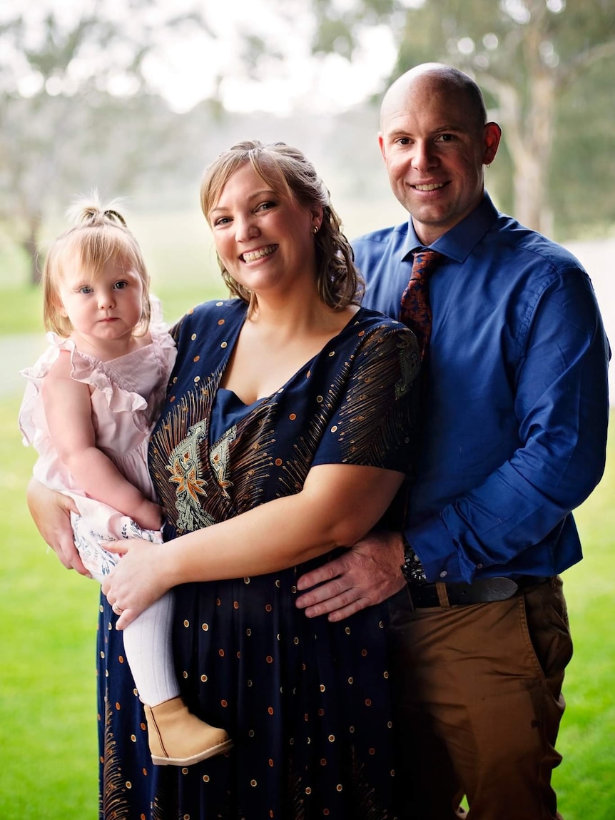 a man, woman, and their young daughter pose for a photo