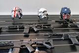 A table with several gel blasters that look like heavy weaponry, as well as some face masks, laid out upon it.