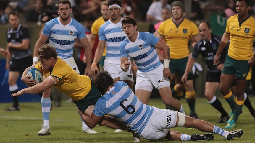 A man wearing yellow dives while holding the ball and being held by a man in a white and blue shirt