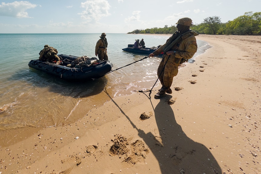 a man in military uniform pulling an inflatable boat to beach shore