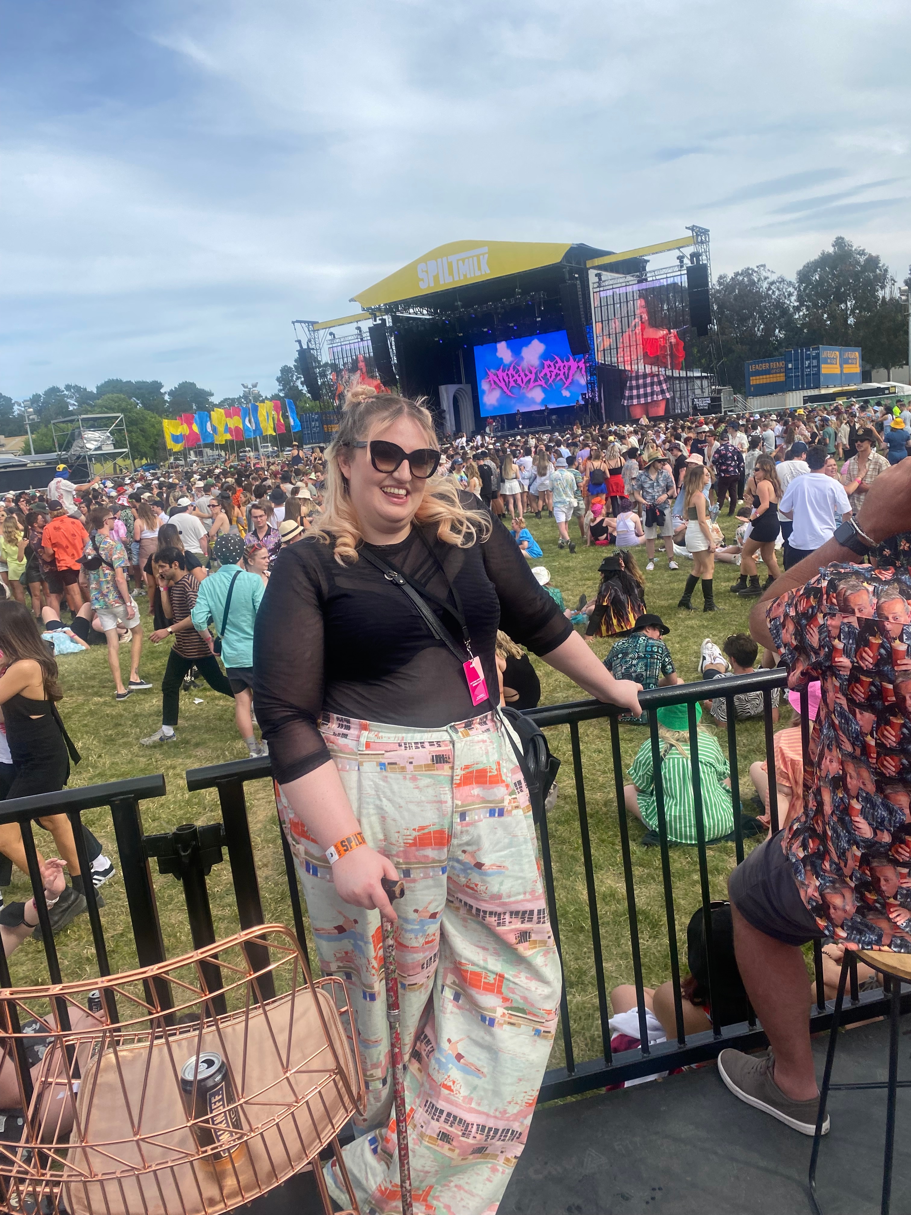 Jovem segurando uma batuta em um festival de música. A cena do Leite Derramado está ao fundo. 