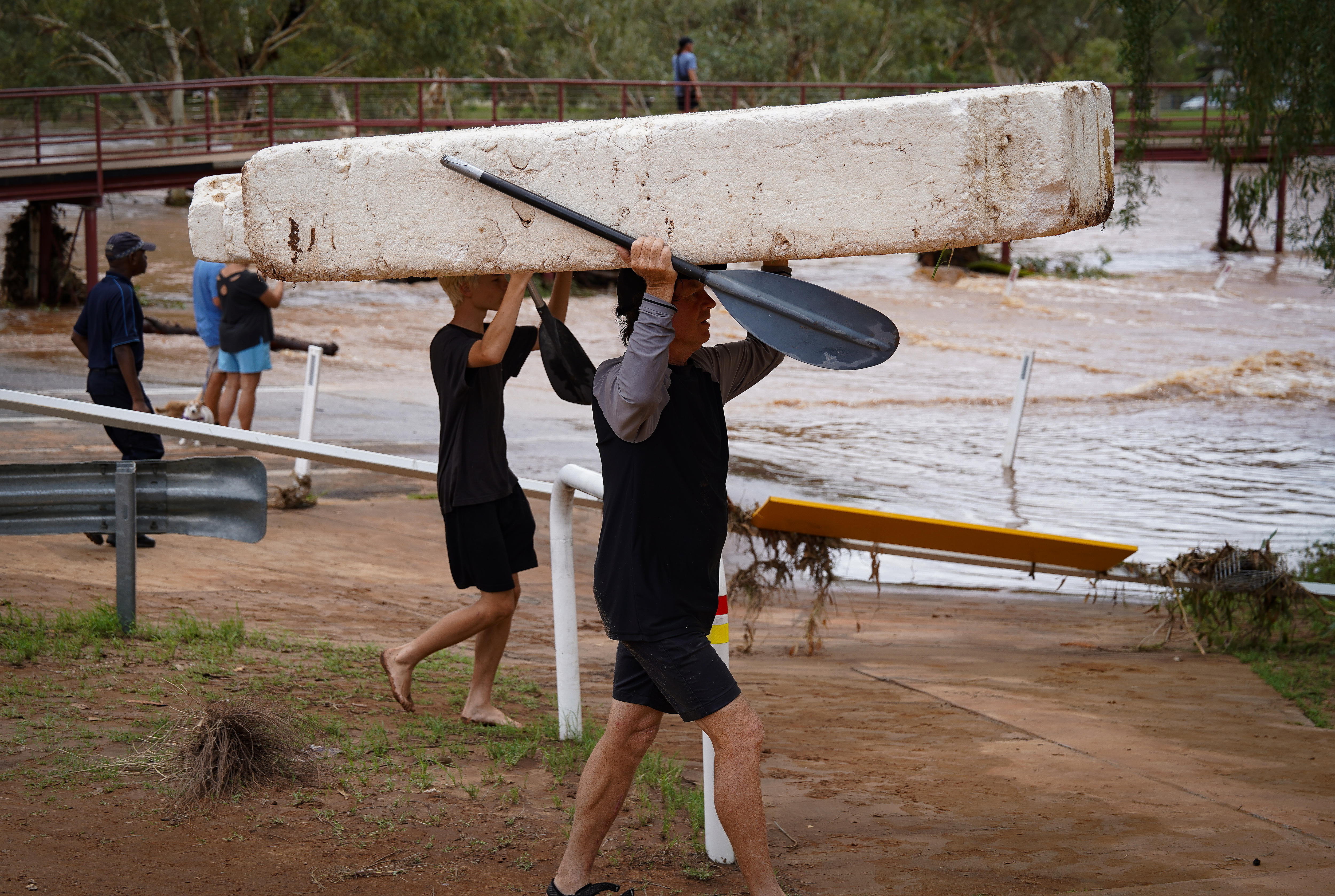 Duas pessoas segurando um grande bloco flutuante e remando em uma canoa enquanto um rio lava a costa atrás. 