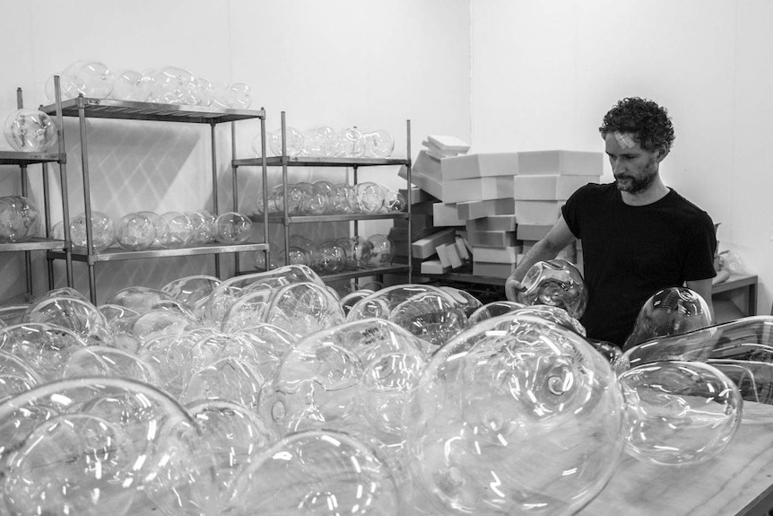 A black and white image of a man standing with a series of glass "bubbles" of different shapes and sizes.