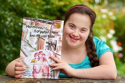Smiling woman with long brown plaited hair holds book title Harmony the Forgetful Hen.