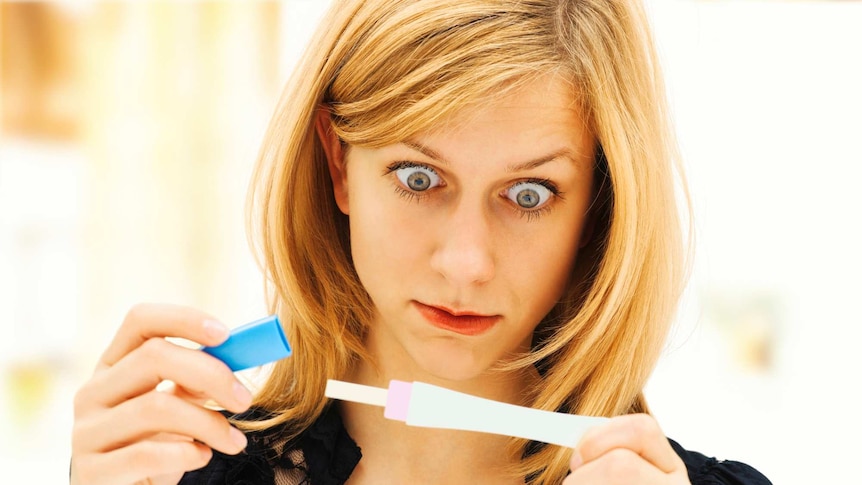 Woman holding a pregnancy test, looking tense, concentrating and shocked