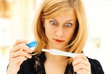 Woman holding a pregnancy test, looking tense, concentrating and shocked