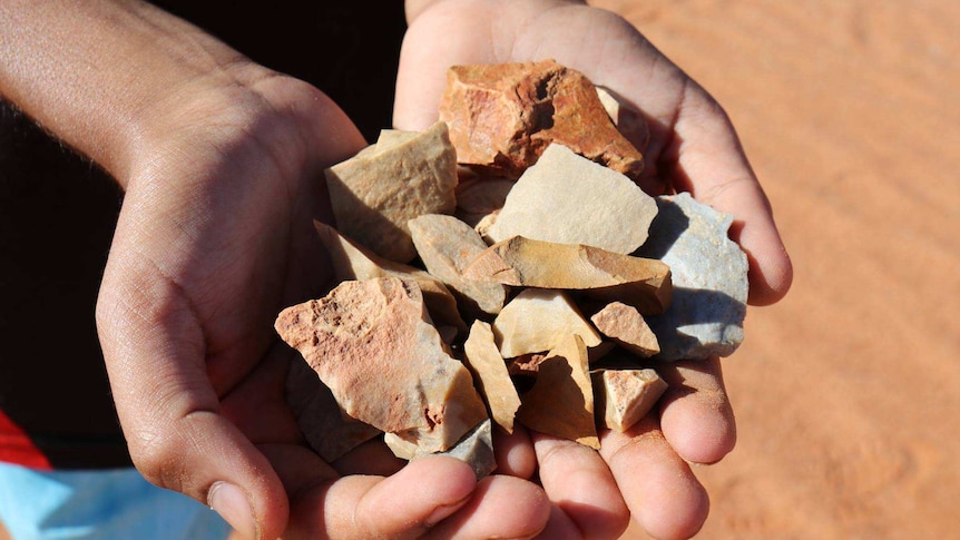 Cupped hands hold flakes of stone coloured red, yellow and grey.