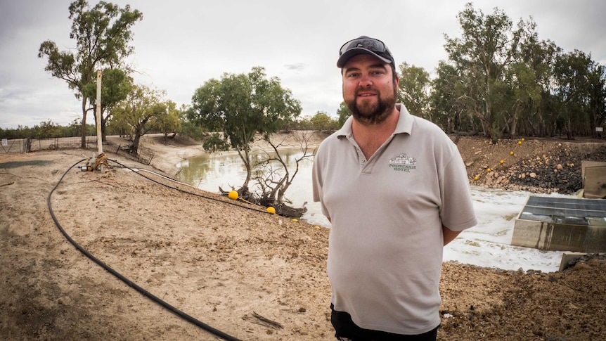 A man in a polo shirt that says Pooncarie Hotel, beaming next to the river at the town's weir.