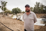 A man in a polo shirt that says Pooncarie Hotel, beaming next to the river at the town's weir.