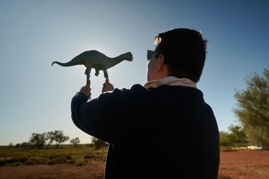Man holding dinosaur sculpture up to sun