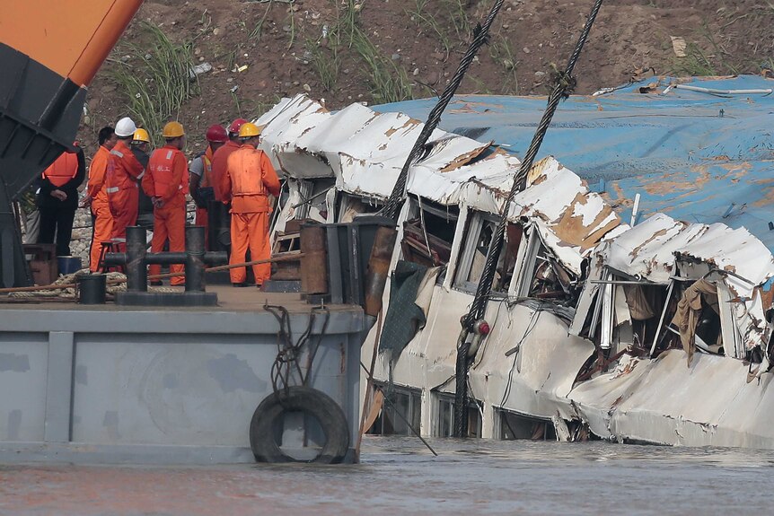 Rescuers stand beside the battered Eastern Star cruise ship
