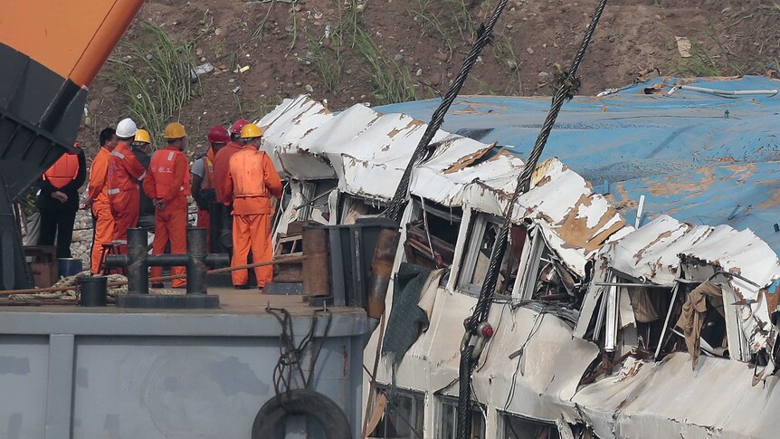 Rescuers stand beside the battered Eastern Star cruise ship