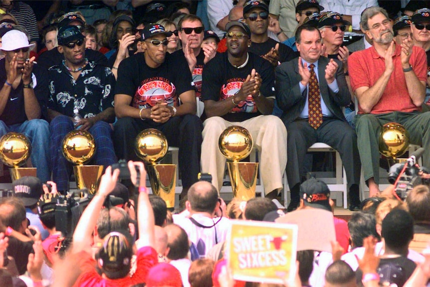 The Chicago Bulls, including Michael Jordan, sit with their NBA championship trophies at a victory parade.