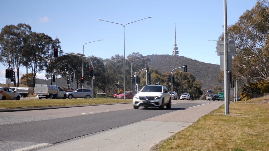 Cars travel along a main road past traffic lights. A large hill with a tower at the top is in the background.