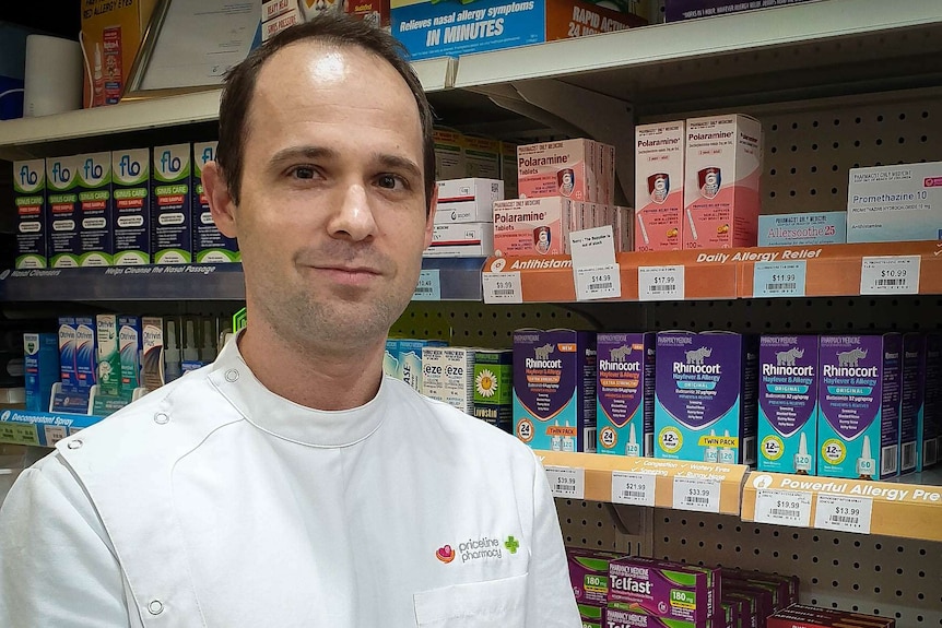 Pharmacist in white coast stands in front of a shelf of medicines