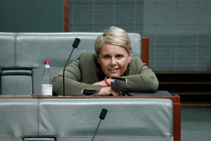 Murphy is leaning forwards onto her desk next to a water bottle. She has short blonde hair.