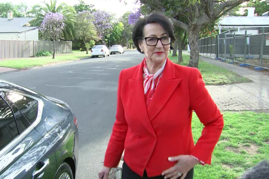 A woman wearing a red blazer next to a car