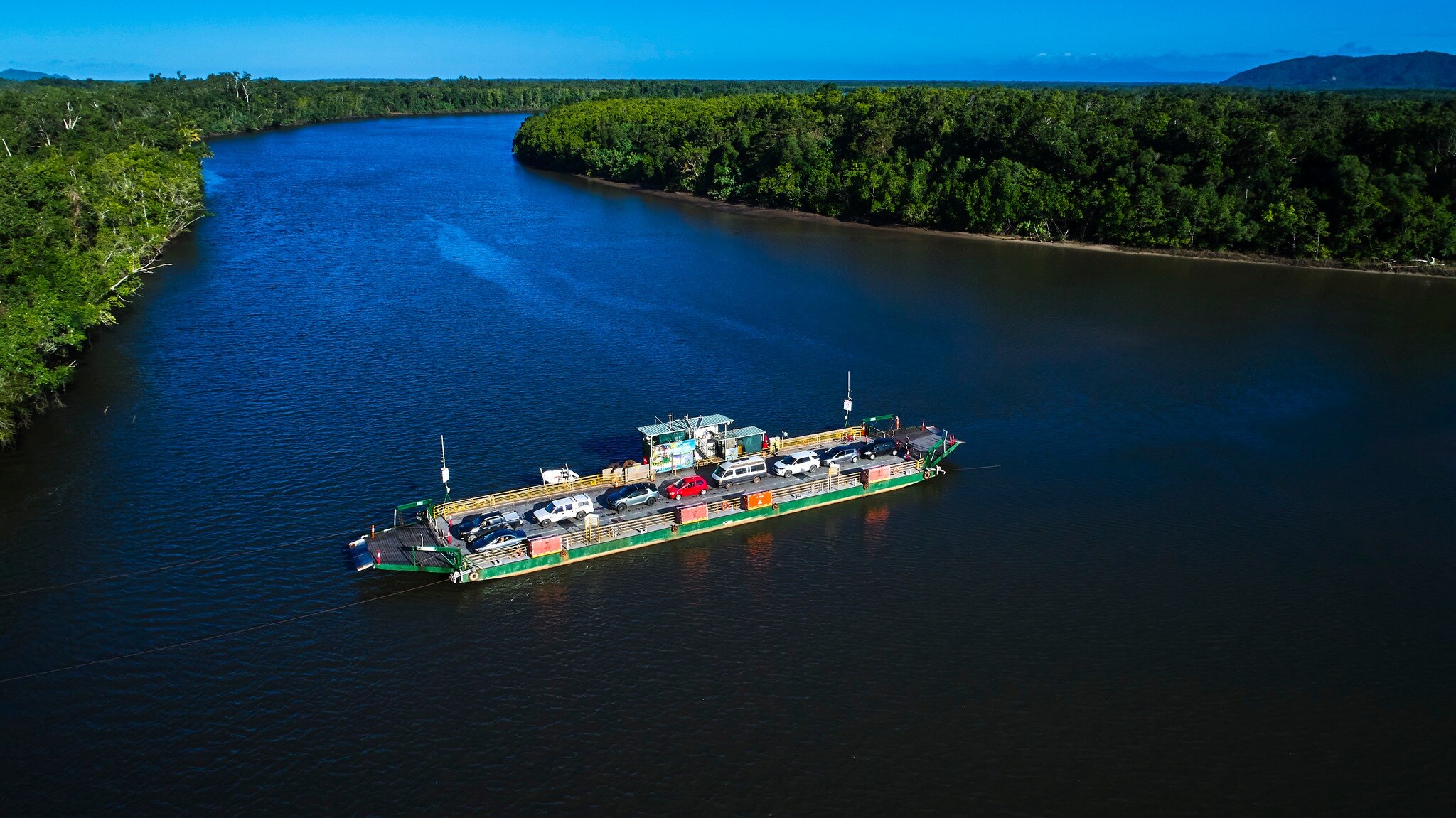 A ferry takes cars down the Daintree River, where the banks of the river overflow with lush green rainforest.