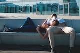 A man and a woman nap on a concrete bench in front of an office building.