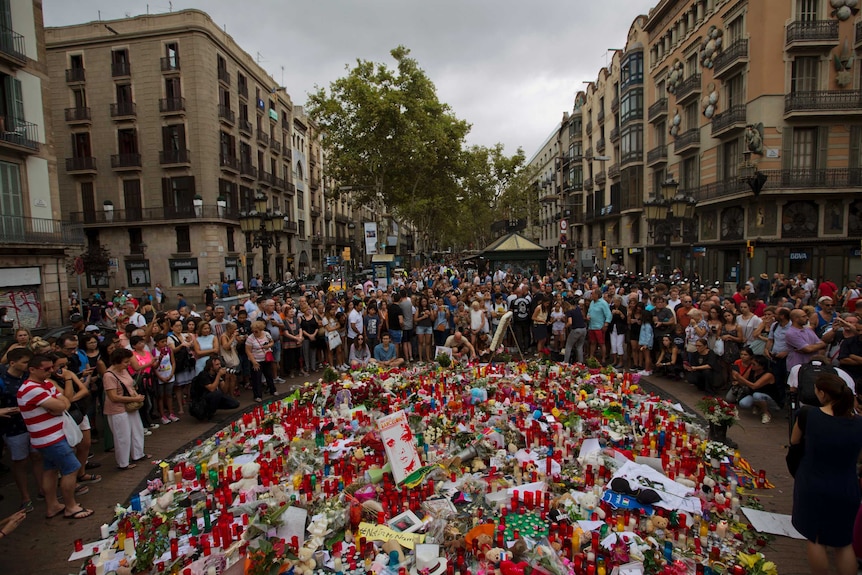 People gather around a memorial tribute of flowers, messages and candles to the victims of the Barcelona attack.