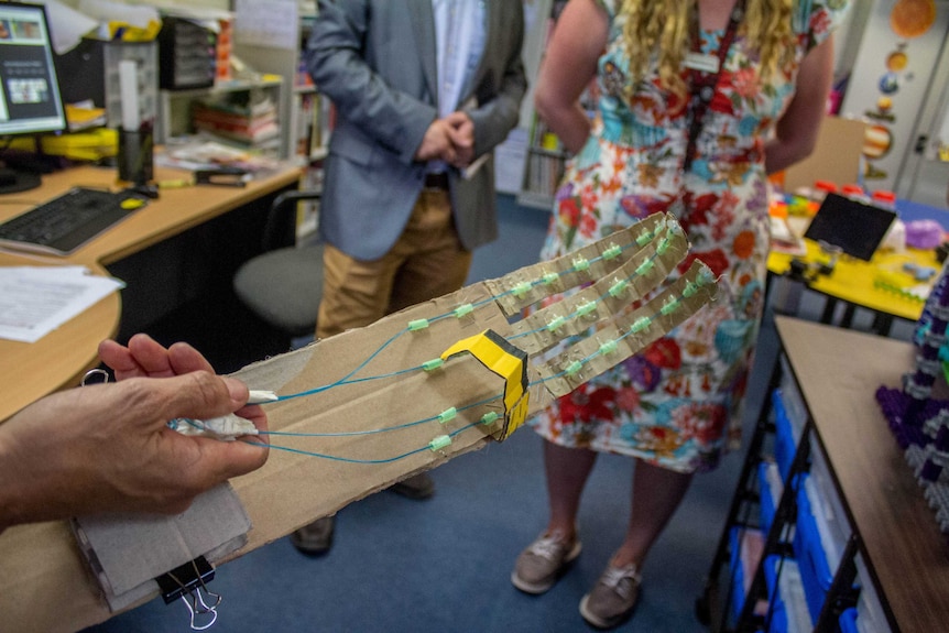 Image of a hand holding a mechanical arm, constructed out of wiring and cardboard.