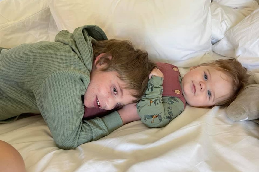 A young boy cuddles his baby brother in bed. 