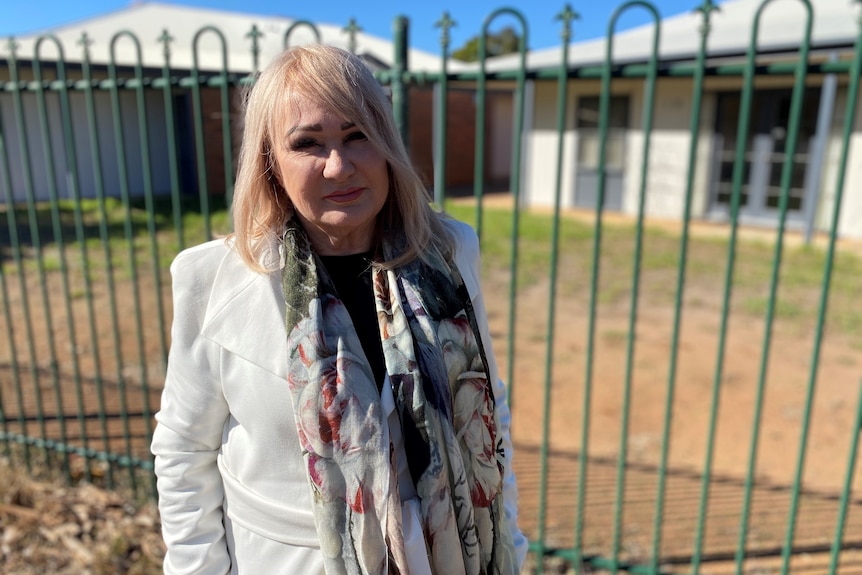 A woman standing in front of a fence with cabins behind