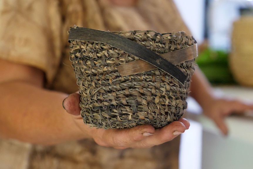 a woman holds a small basket that's been hand woven with vine