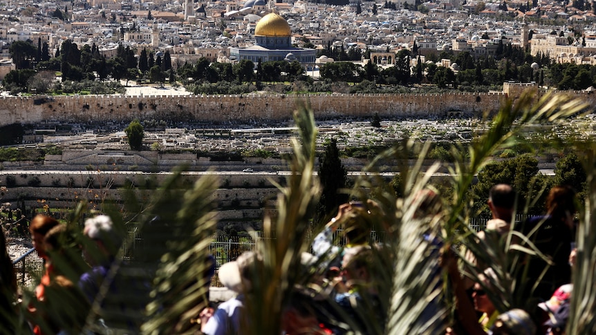 The Dome of the Rock is seen in the background as Christian worshippers attend a Palm Sunday procession.