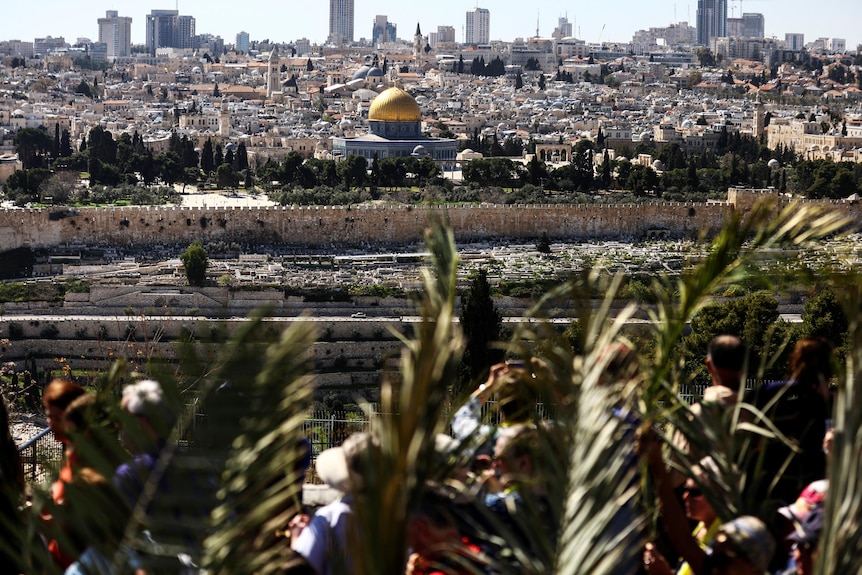 The Dome of the Rock is seen in the background as Christian worshippers attend a Palm Sunday procession.