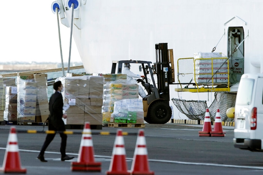 You view a forklift loading a crate of supplies to the side of a white ship with a supply door open.