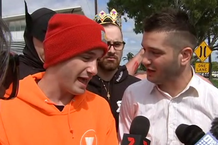 A man wearing an orange jumper and red beanie standing next to a man wearing a white shirt