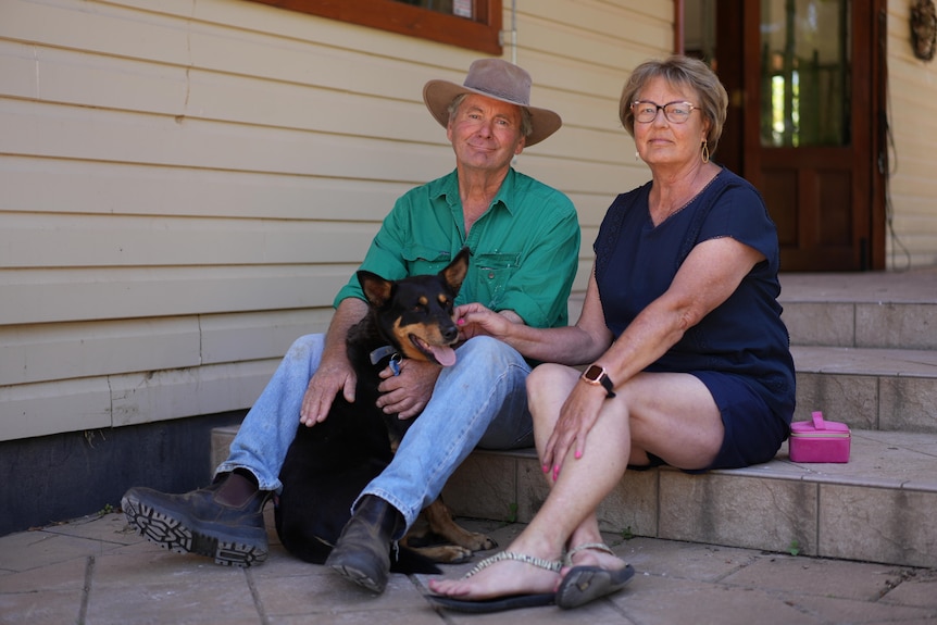 Man and woman sitting on the steps of a house with a black cattle dog. 