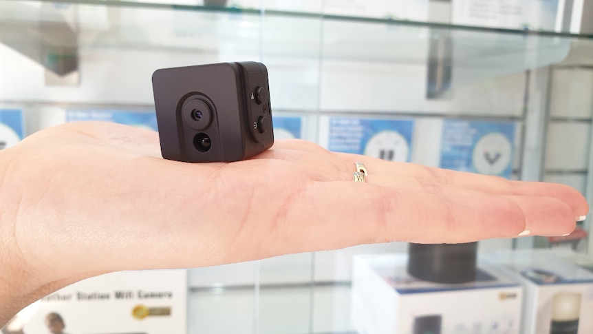 A small, black, square camera sits in the palm of a hand.