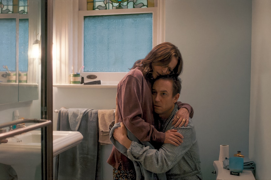 Julia Louis-Dreyfus, a middle-aged brunette woman, and Tobias Menzies, a middle-aged fair-haired man, embrace in a bathroom.