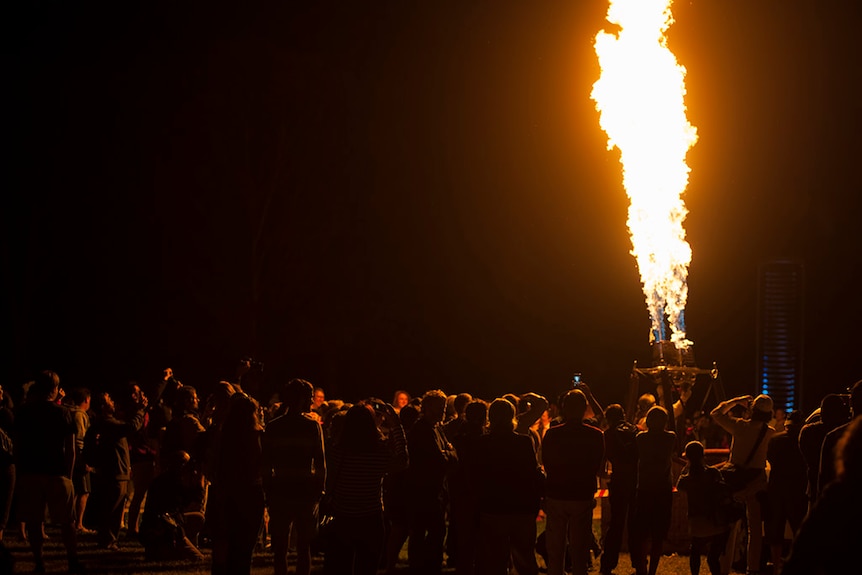 People watch on as fire is blasted from a hot air balloon in the dark.