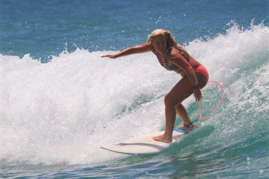 Young girl with blonde hair surfing on a blue and white wave on a sunny da