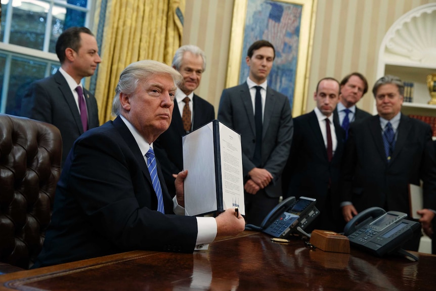 President Donald Trump shows off a signed executive order in the Oval Office.